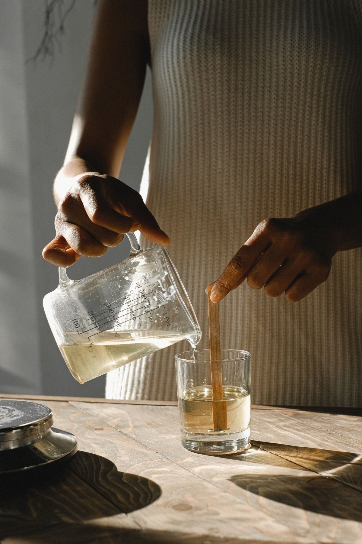 A Black woman's hands pouring wax into candles with wooden wicks