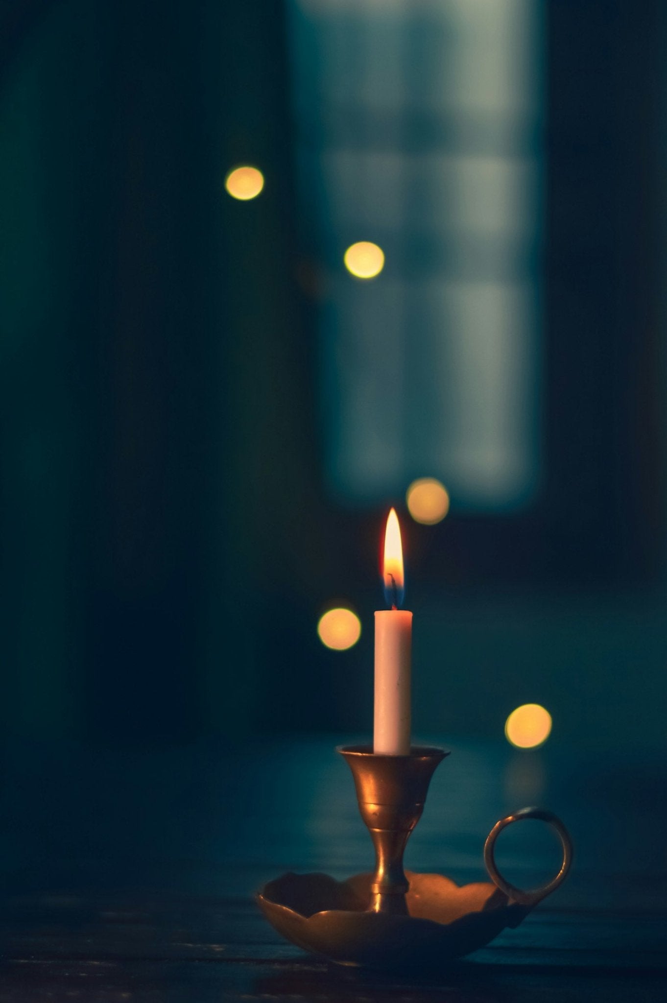 A white candle lit on a brass candle holder in the dark