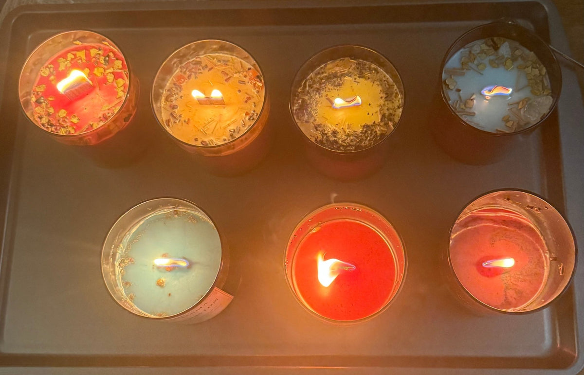 Seven Geechee Mama Hoodoo candles burning on a tray in red, gold, yellow, white, blue, orange, and pink, each fixed with herbs and stones