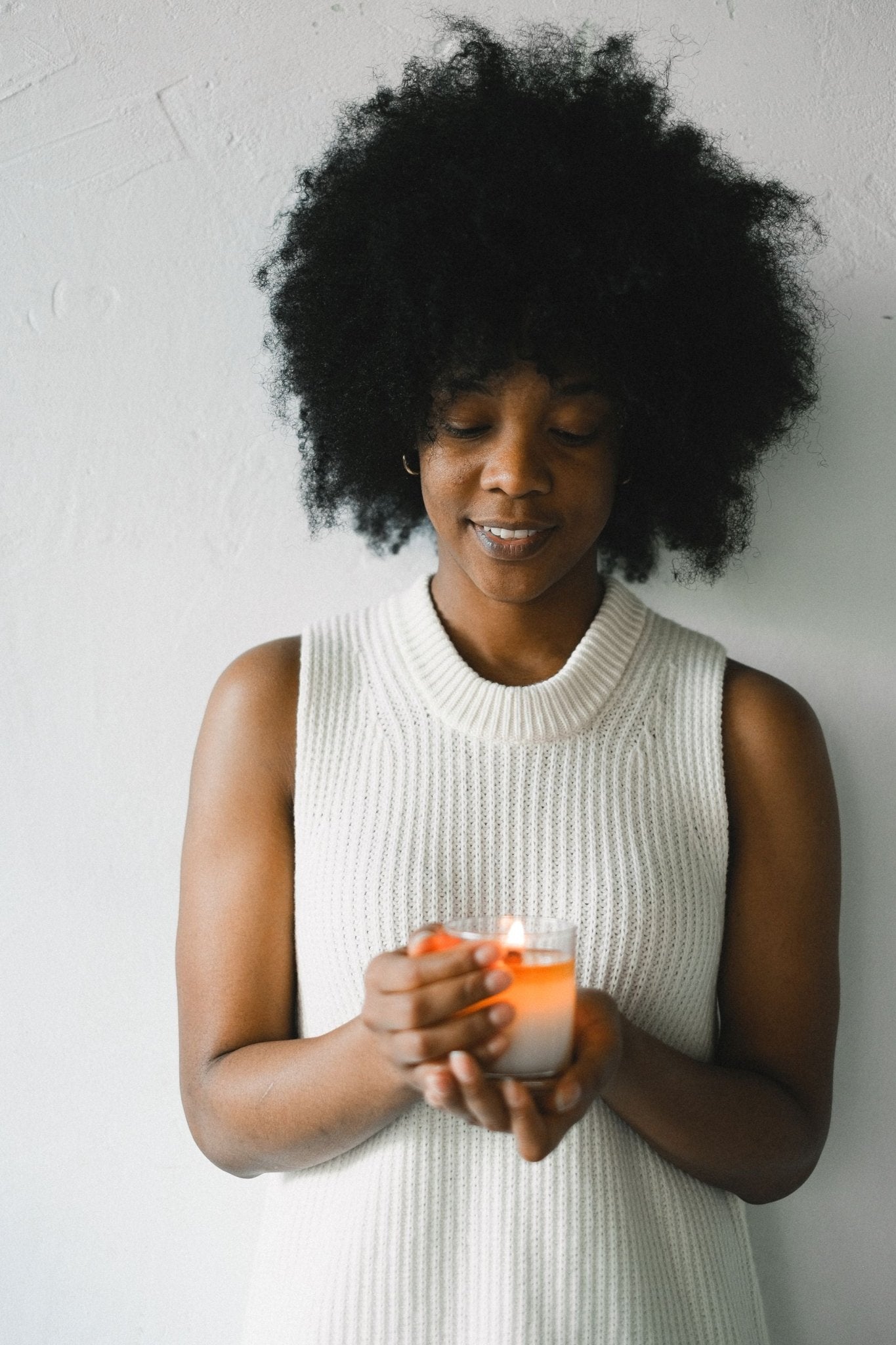 A Black woman holding a lit candle in glass, a light set over the work
