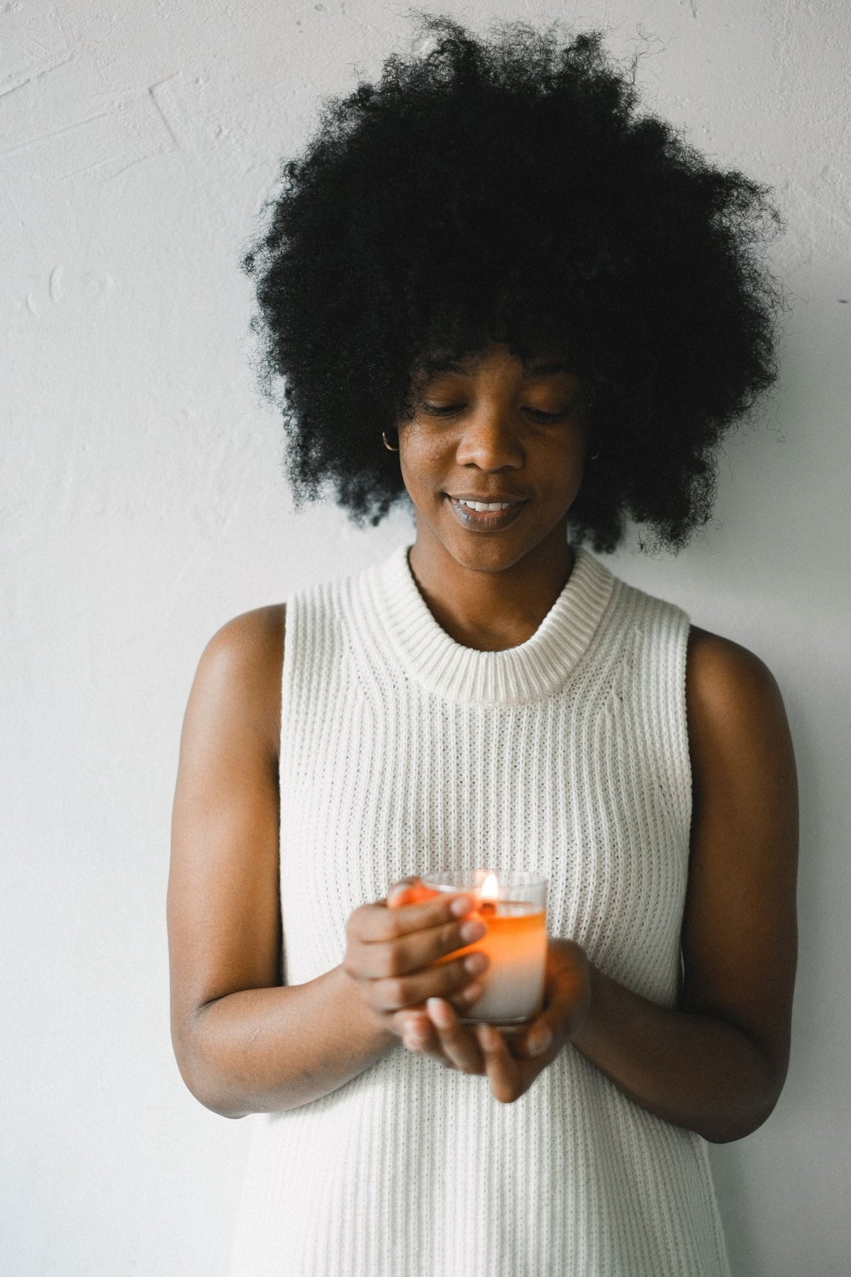 A Black woman holding a lit candle in glass, a light set over the work