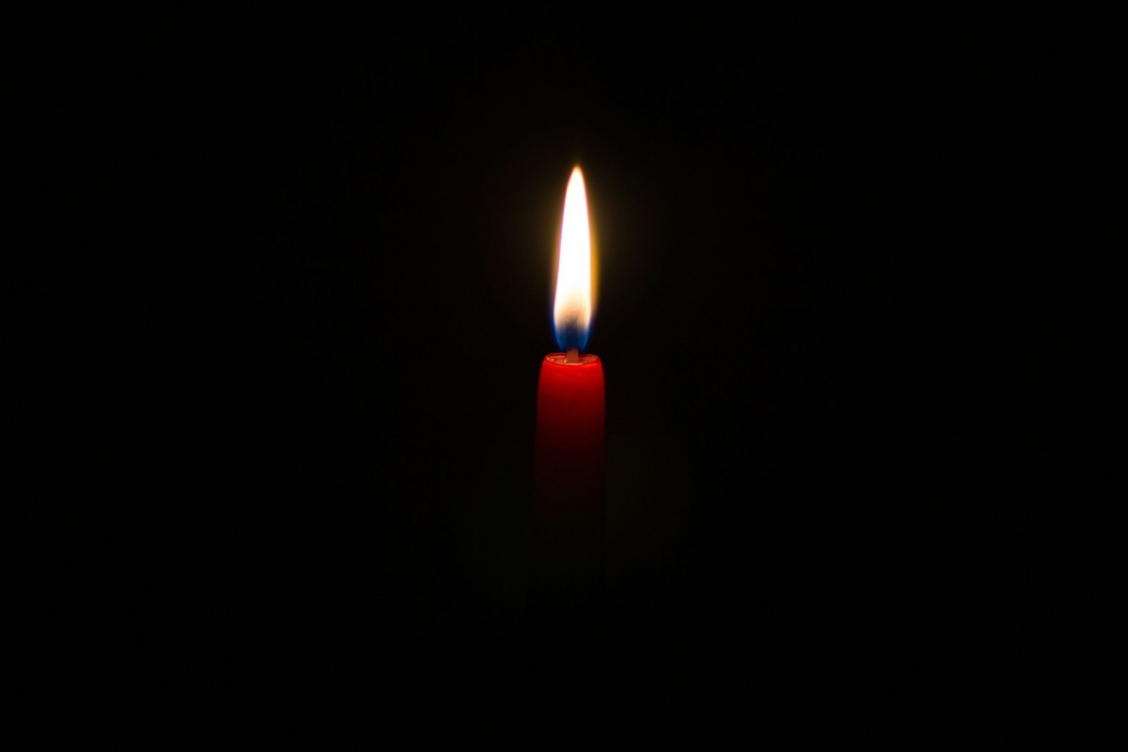 A lit red candle glowing against a dark background | Geechee Mama