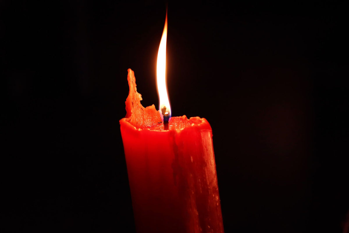 A red candle burning against a dark background, the color of love and courage in Hoodoo candle work