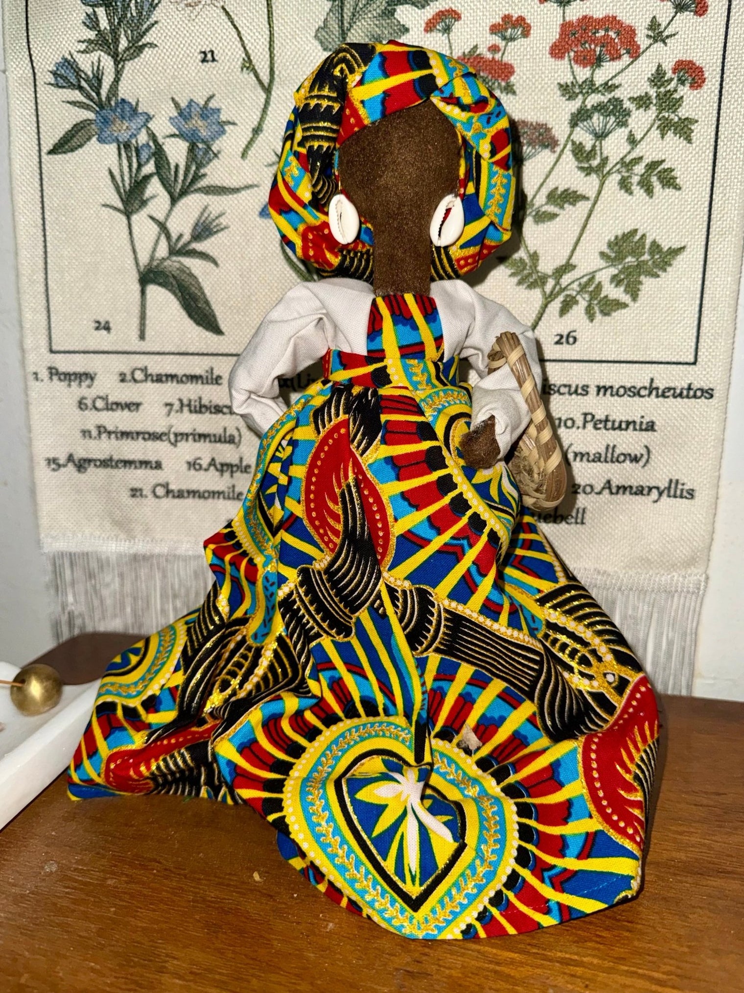 A handmade faceless Gullah doll in a bright wax print gown and matching headwrap, wearing cowrie shell earrings